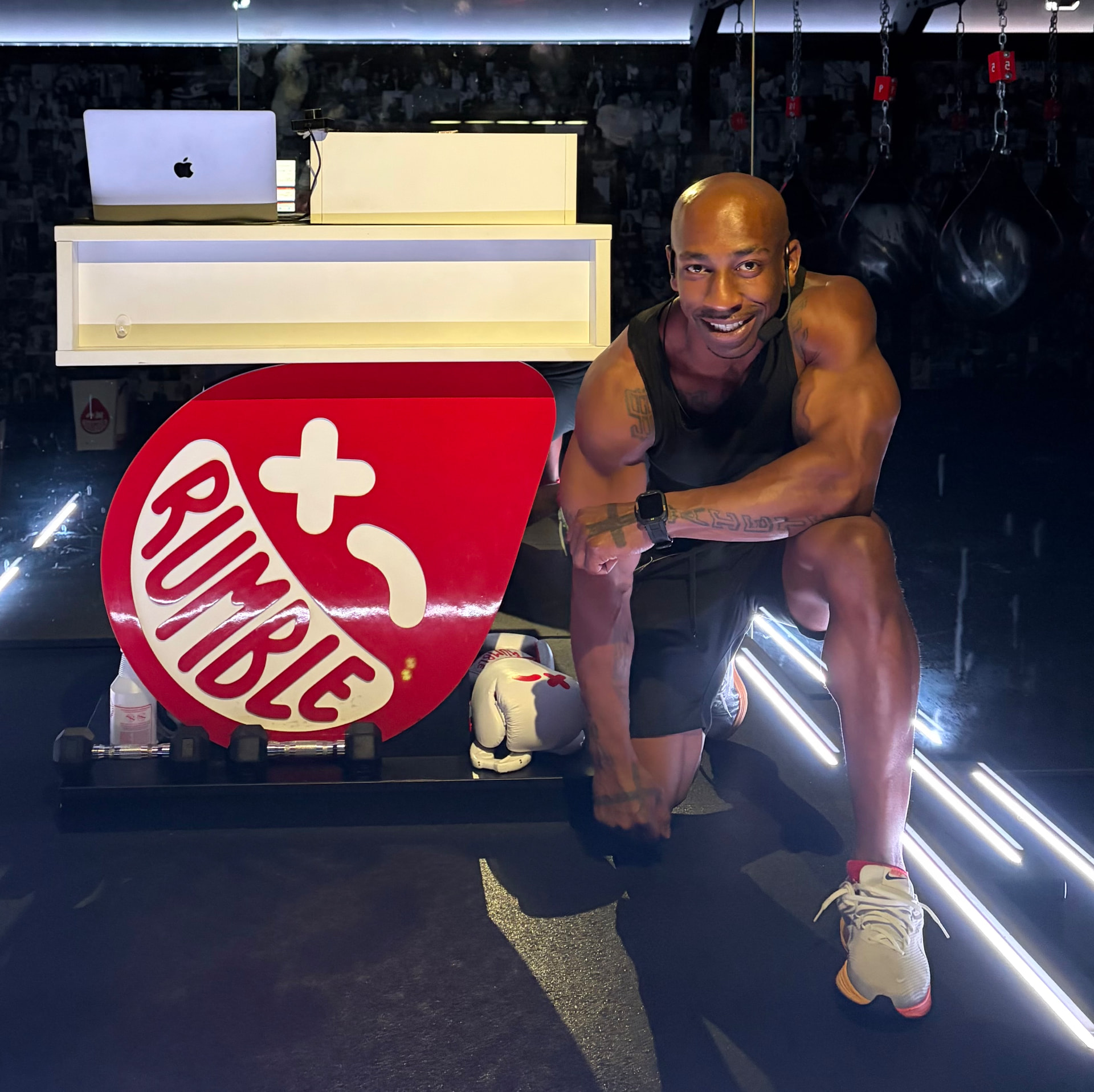 Coach Asa kneeling beside the Rumble Boxing sign